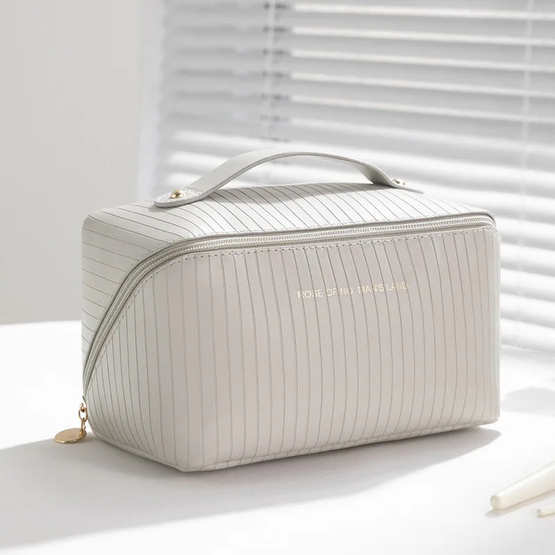 Elegante borsa cosmetica bianca a righe verticali, con manico superiore e cerniera dorata, su sfondo luminoso. Accessorio da viaggio chic.