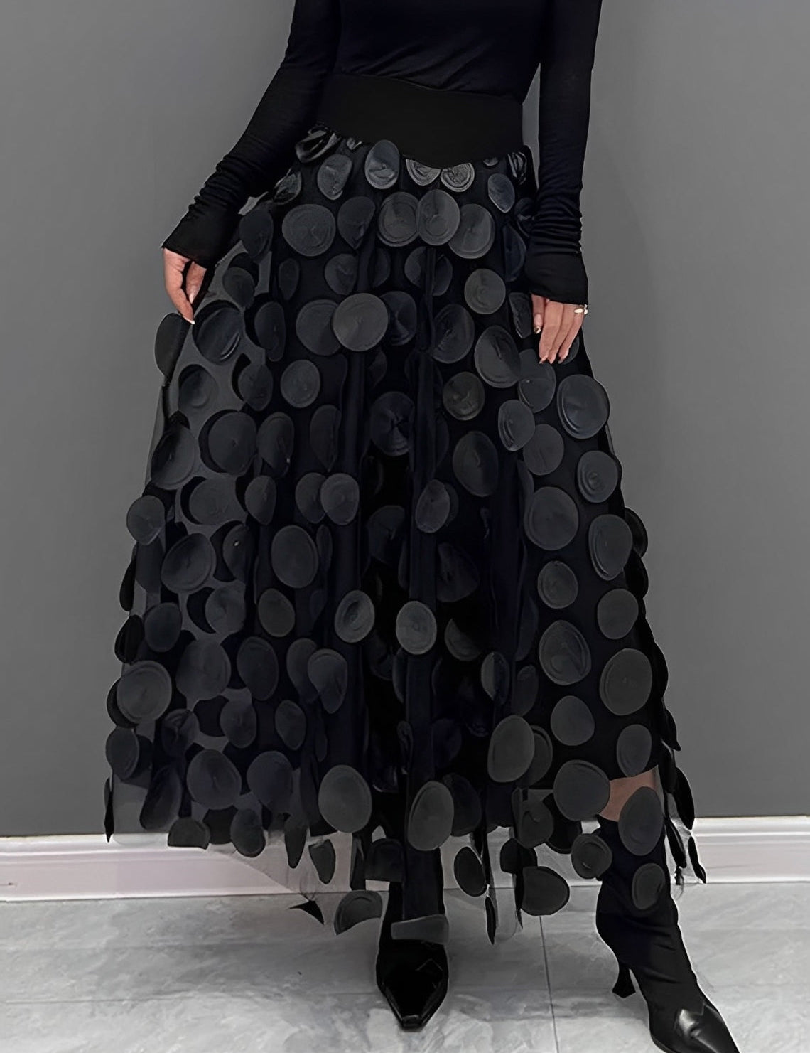 Donna con gonna nera a pois 3D, top nero a maniche lunghe, scarpe nere a punta. Moda elegante, abbigliamento femminile, stile contemporaneo.