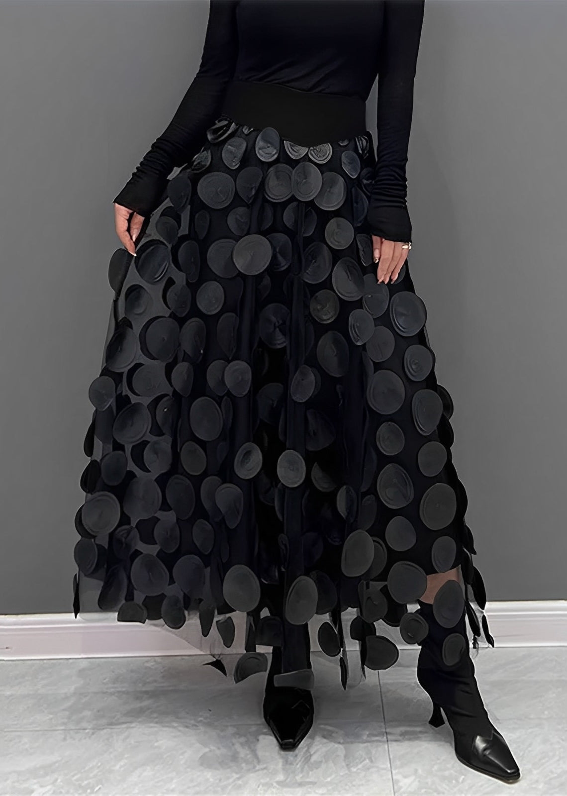 Donna con gonna nera a pois 3D, top nero a maniche lunghe, scarpe nere a punta. Moda elegante, abbigliamento femminile, stile contemporaneo.