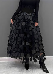 Donna con gonna nera a pois 3D, top nero a maniche lunghe, scarpe nere a punta. Moda elegante, abbigliamento femminile, stile contemporaneo.