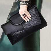 Borsa a mano nera in pelle con texture pitonata, chiusura a patta, indossata da una donna elegante. Accessorio moda di lusso.