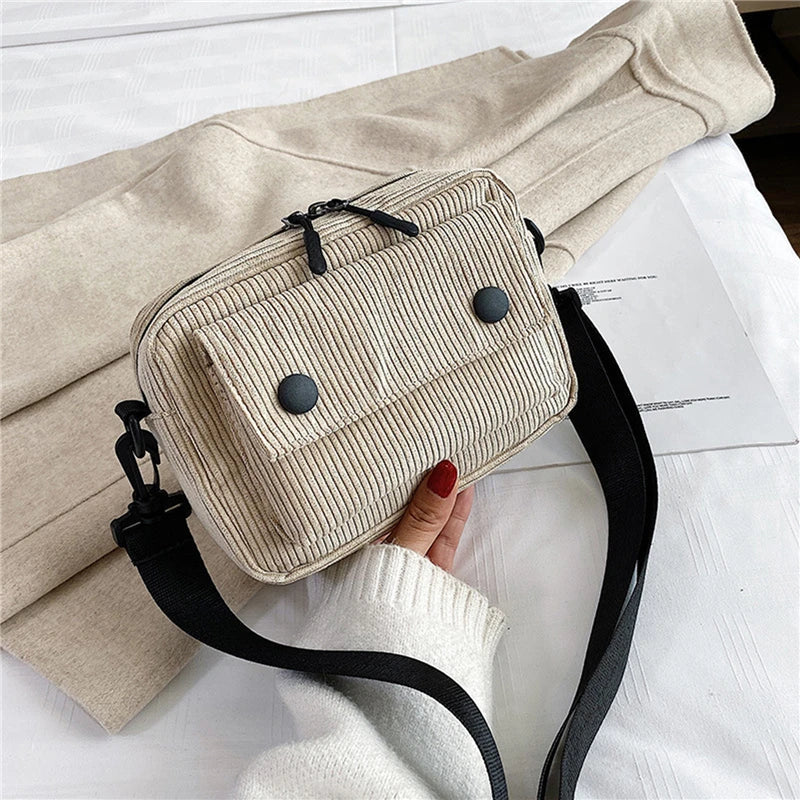 Borsa a tracolla beige in tessuto a coste con tasche frontali e cerniera, manico nero regolabile, su sfondo chiaro. Accessorio moda casual.