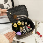 Borsa cosmetica aperta con flaconi di profumo, pennelli trucco e prodotti skincare. Organizer da viaggio elegante e capiente per cosmetici.