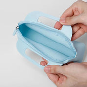 Mani che tengono un astuccio azzurro in silicone con cerniera aperta, design moderno e manici integrati. Accessorio pratico per scuola o ufficio.