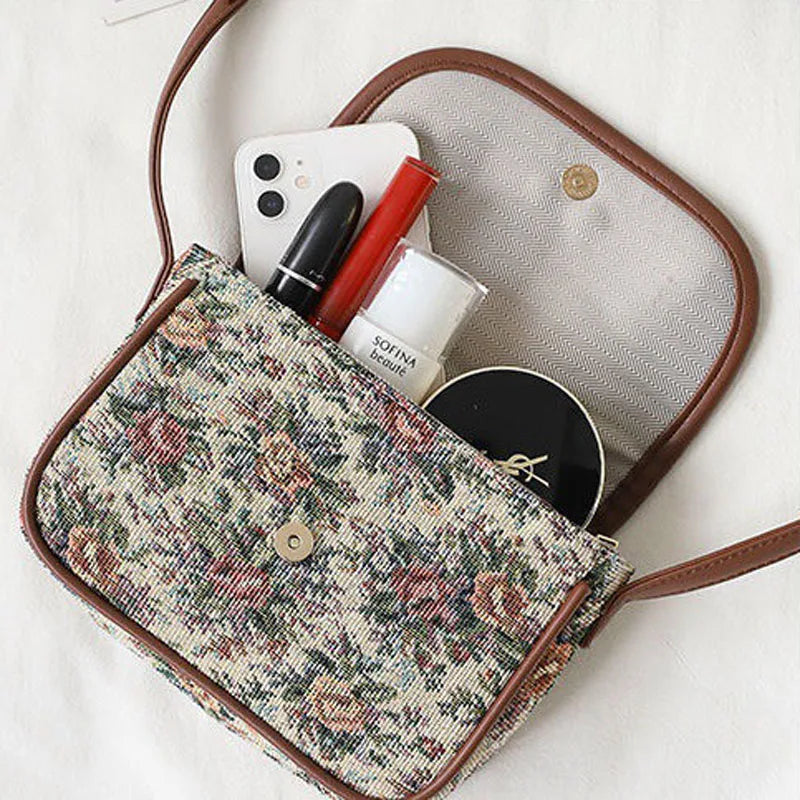 Borsa a tracolla floreale aperta con smartphone, rossetto, cipria e crema. Accessori moda donna, stile vintage, eleganza quotidiana.