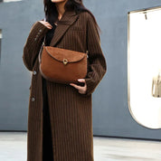 Cappotto lungo a righe marroni con borsa a tracolla in pelle marrone, chiusura a fibbia dorata. Moda autunnale elegante per donna.