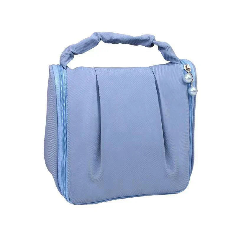 Borsa cosmetica da viaggio blu con manico intrecciato, chiusura a zip e decorazione con perle. Ideale per organizzare trucchi e accessori.