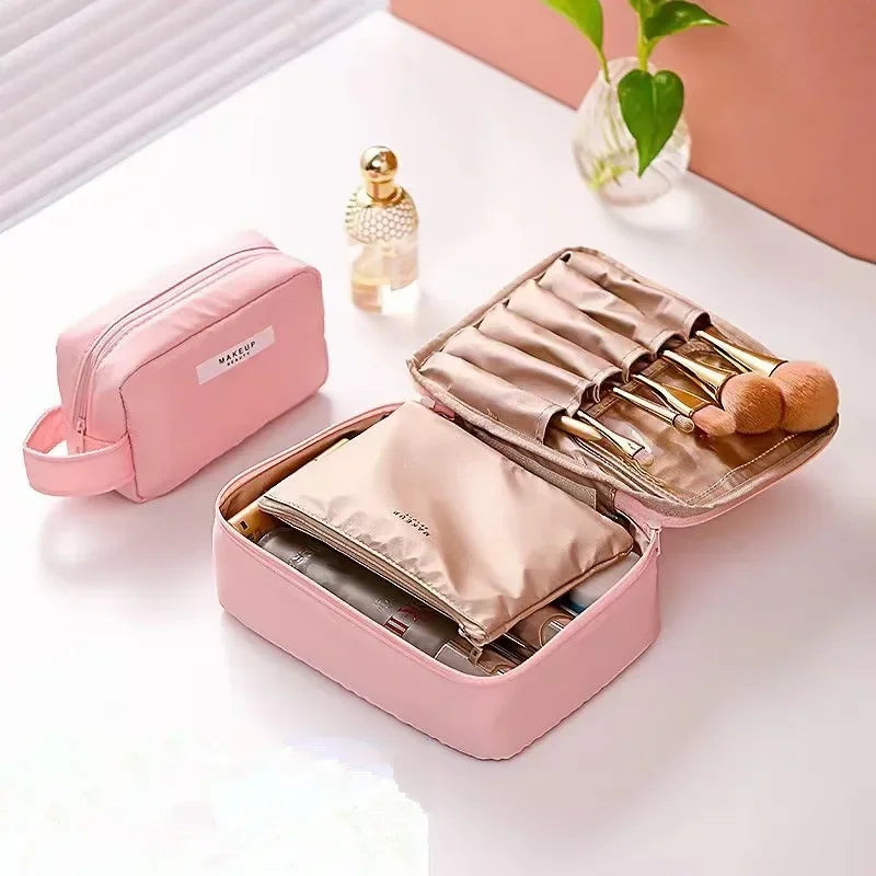 Astuccio trucco rosa aperto con pennelli e cosmetici, accanto a una boccetta di profumo e una pianta. Organizzatore da viaggio elegante e funzionale.