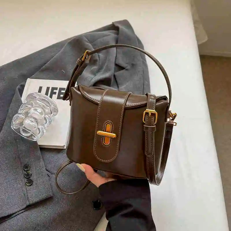 Borsa a tracolla in pelle marrone su giacca grigia, con bicchiere e rivista. Elegante accessorio moda donna, stile casual chic.