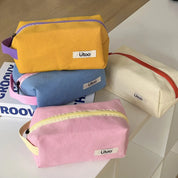 Quattro astucci colorati in tessuto con cerniera, marchio Utoo, su tavolo bianco. Colori: giallo, blu, rosa, crema. Accessori scuola, organizer.