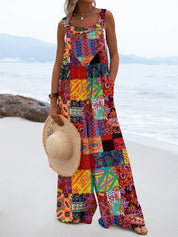 Donna in spiaggia con tuta lunga patchwork colorata, cappello di paglia in mano. Moda estiva, abbigliamento boho chic, abito casual vivace.