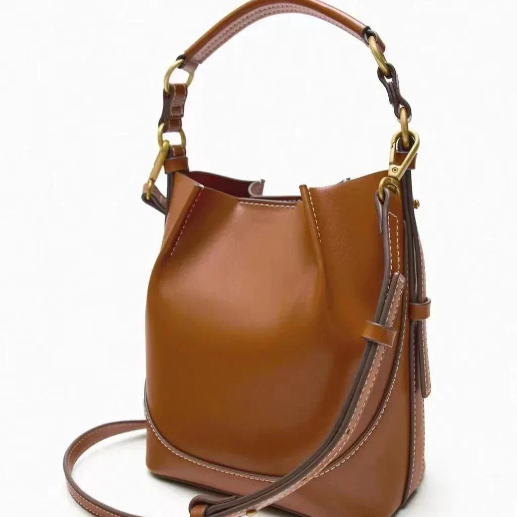 Borsa a secchiello in pelle marrone con tracolla regolabile, dettagli in metallo dorato, design elegante e moderno. Accessorio moda donna.