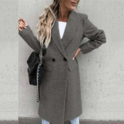 Donna con cappotto grigio elegante, doppio petto, indossa jeans chiari e borsa nera a tracolla. Moda autunnale, stile casual chic.
