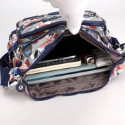 Borsa a tracolla floreale aperta, mostra tasche multiple con notebook, penne e accessori. Design colorato, ideale per organizzazione e stile.