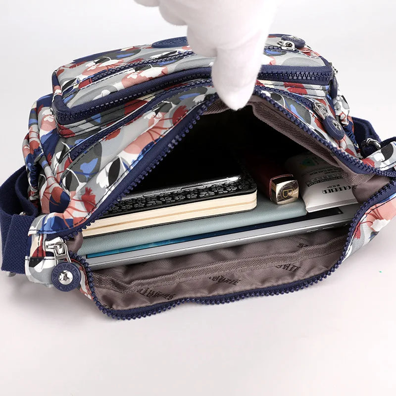 Borsa a tracolla floreale aperta, mostra tasche multiple con notebook, penne e accessori. Design colorato, ideale per organizzazione e stile.