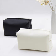 Due astucci in pelle sintetica, uno nero e uno bianco, su sfondo bianco con vaso di fiori. Eleganti e pratici per cosmetici o accessori da viaggio.