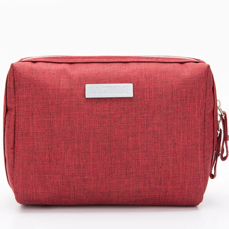 Astuccio da viaggio rosso in tessuto, con cerniera e targhetta argentata. Ideale per organizzare accessori e cosmetici. Design compatto e moderno.