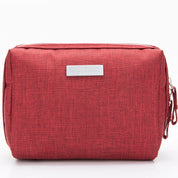 Astuccio da viaggio rosso in tessuto, con cerniera e targhetta argentata. Ideale per organizzare accessori e cosmetici. Design compatto e moderno.