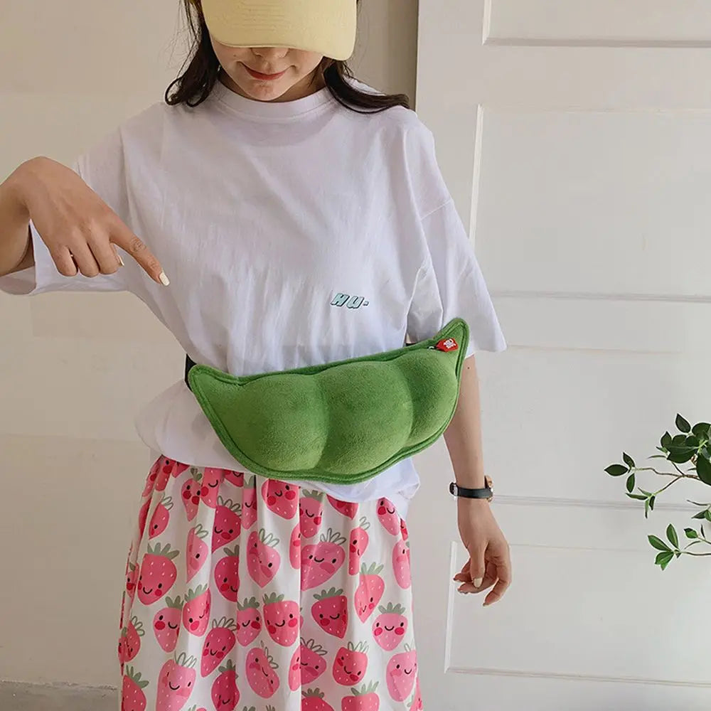 Donna con marsupio verde a forma di baccello di piselli, indossa maglietta bianca e gonna con fragole. Accessorio moda originale e divertente.