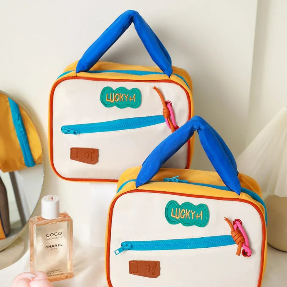 Due borse termiche colorate con manici blu, tasche con cerniera e dettagli decorativi, accanto a una bottiglia di profumo Chanel Coco.