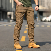 Pantaloni cargo uomo marroni, tasche multiple, indossati con stivali gialli su strada urbana. Moda casual maschile, abbigliamento outdoor.