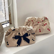 Due pochette in tessuto beige con fiocchi, una blu e una rosa, e motivi a pois rossi e neri, su un davanzale vicino a una finestra.