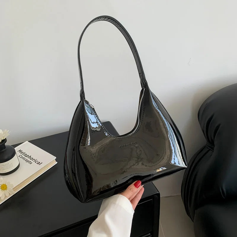 Borsa a spalla nera lucida in pelle sintetica, design moderno, manico singolo, su tavolo con decorazioni minimaliste. Accessorio moda elegante.