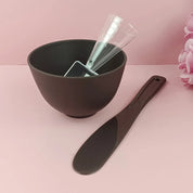 Ciotola nera per maschera viso con spatola e misurino trasparente su sfondo rosa. Accessori per cura della pelle, bellezza, cosmetici.