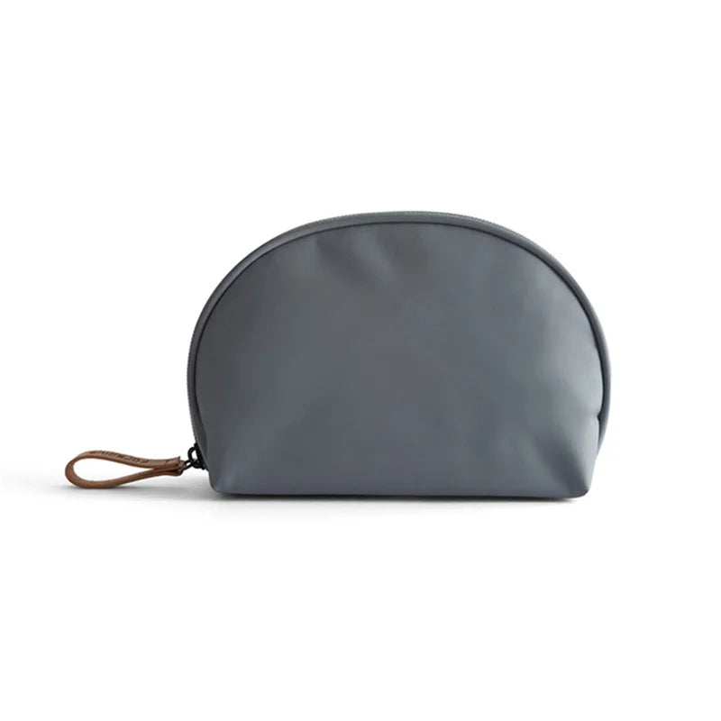 Borsa cosmetica grigia in pelle sintetica, design a mezzaluna, con cerniera e manico in pelle marrone. Accessorio elegante e pratico per viaggio.