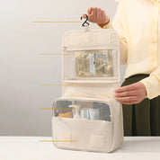 Borsa da viaggio beige appesa, con scomparti trasparenti e tasche a rete, ideale per organizzare cosmetici e articoli da toeletta.