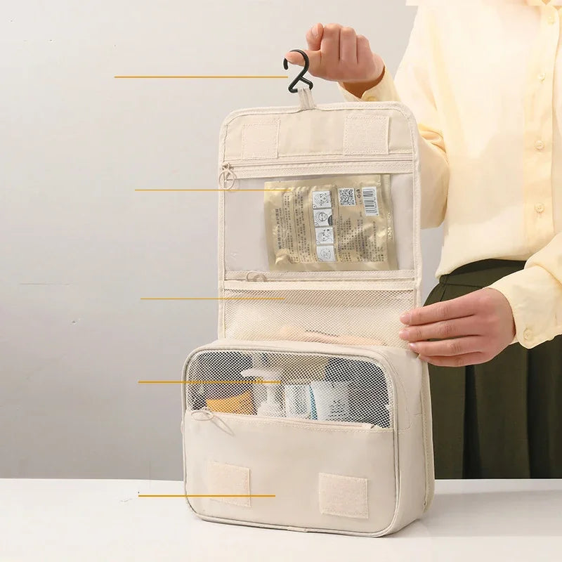 Borsa da viaggio beige appesa, con scomparti trasparenti e tasche a rete, ideale per organizzare cosmetici e articoli da toeletta.
