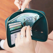 Portafoglio verde in pelle aperto con cerniera, contenente banconote, carte di credito e monete. Mani femminili con anello elegante.