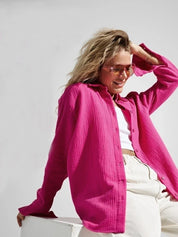 Donna con camicia rosa acceso, occhiali da sole, top bianco e pantaloni chiari. Moda estiva, abbigliamento casual, stile trendy.