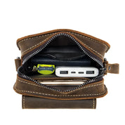 Borsa in pelle marrone aperta, contenente power bank, portafoglio, chiavi e caramella Doublemint. Accessori organizzati per viaggio e uso quotidiano.