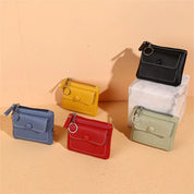 Cinque portamonete in pelle colorata: nero, giallo, blu, rosso e verde, con cerniera e anello portachiavi, su sfondo beige. Accessori moda eleganti.