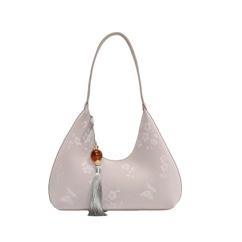 Borsa a spalla elegante in pelle beige con motivo floreale, decorata con nappina e perla. Accessorio moda donna, stile chic e raffinato.