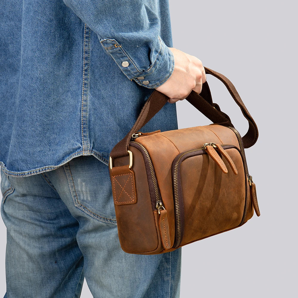 Uomo con camicia di jeans che tiene una borsa a tracolla in pelle marrone, design vintage, tasche con cerniera, moda casual, accessorio maschile.