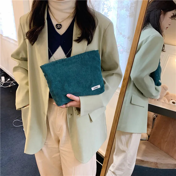 Donna con blazer verde chiaro, maglione blu, pantaloni beige, tiene una pochette verde. Moda casual elegante, abbigliamento autunnale femminile.