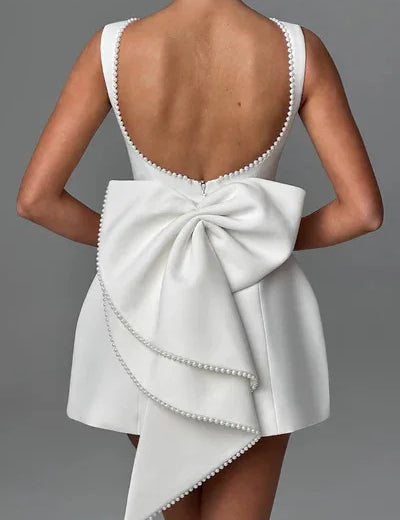 Abito bianco elegante con schiena scoperta e grande fiocco posteriore, decorato con perline. Perfetto per cerimonie e occasioni speciali.