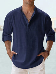 Camicia uomo blu scuro in lino, maniche lunghe, colletto alla coreana, abbinata a pantaloni bianchi. Stile casual elegante per moda estiva.
