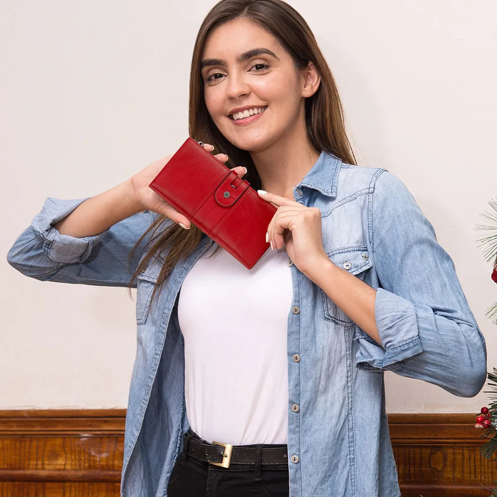 Donna sorridente con camicia di jeans tiene portafoglio rosso in pelle. Accessorio moda elegante, ideale per regali natalizi.