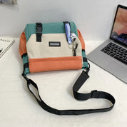 Borsa a tracolla multicolore su scrivania con laptop, libro e portachiavi. Design moderno, ideale per lavoro e scuola. Accessorio moda unisex.