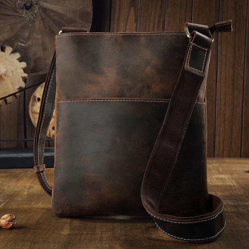 Borsa a tracolla in pelle marrone vintage su tavolo di legno, design elegante e resistente, ideale per uomo, accessorio moda casual.