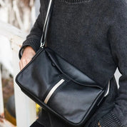 Borsa a tracolla in pelle nera, design elegante con striscia centrale, indossata da persona in maglione grigio. Accessorio moda uomo/donna.