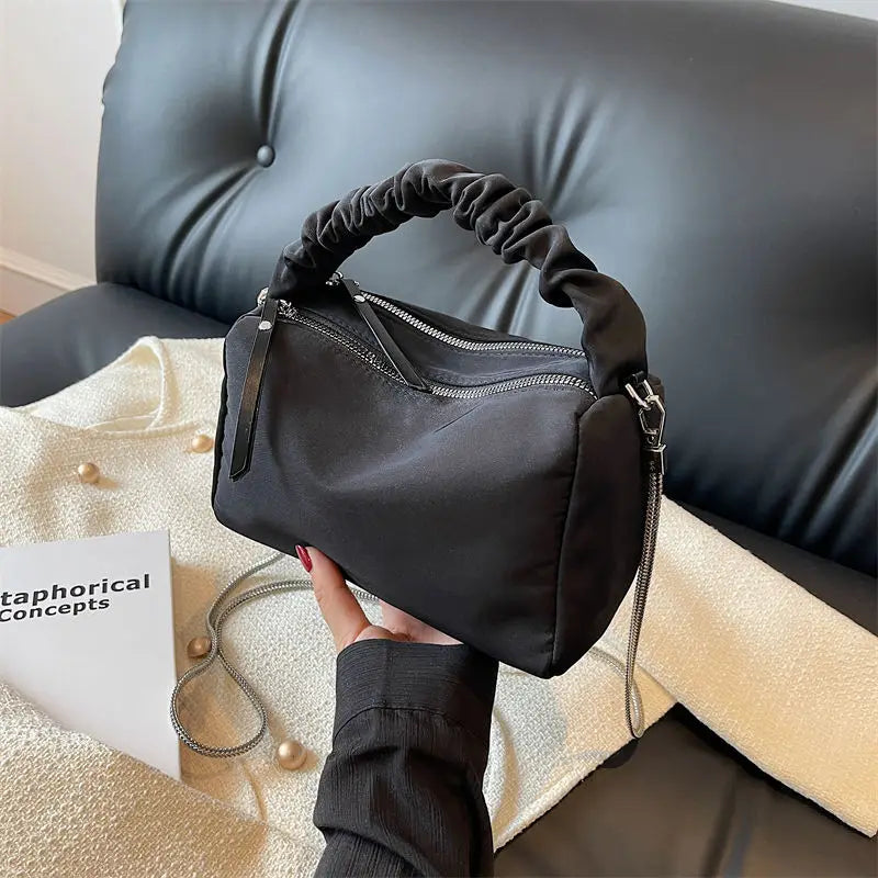 Borsa a mano nera in tessuto con manico arricciato, zip argentata, su divano nero. Accessorio moda elegante e versatile per donna.