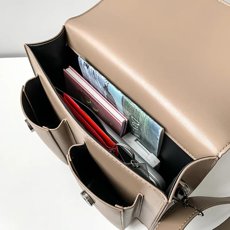 Borsa a tracolla beige aperta, con libri e accessori all'interno. Design elegante, ideale per lavoro e scuola. Tasche multiple per organizzazione.