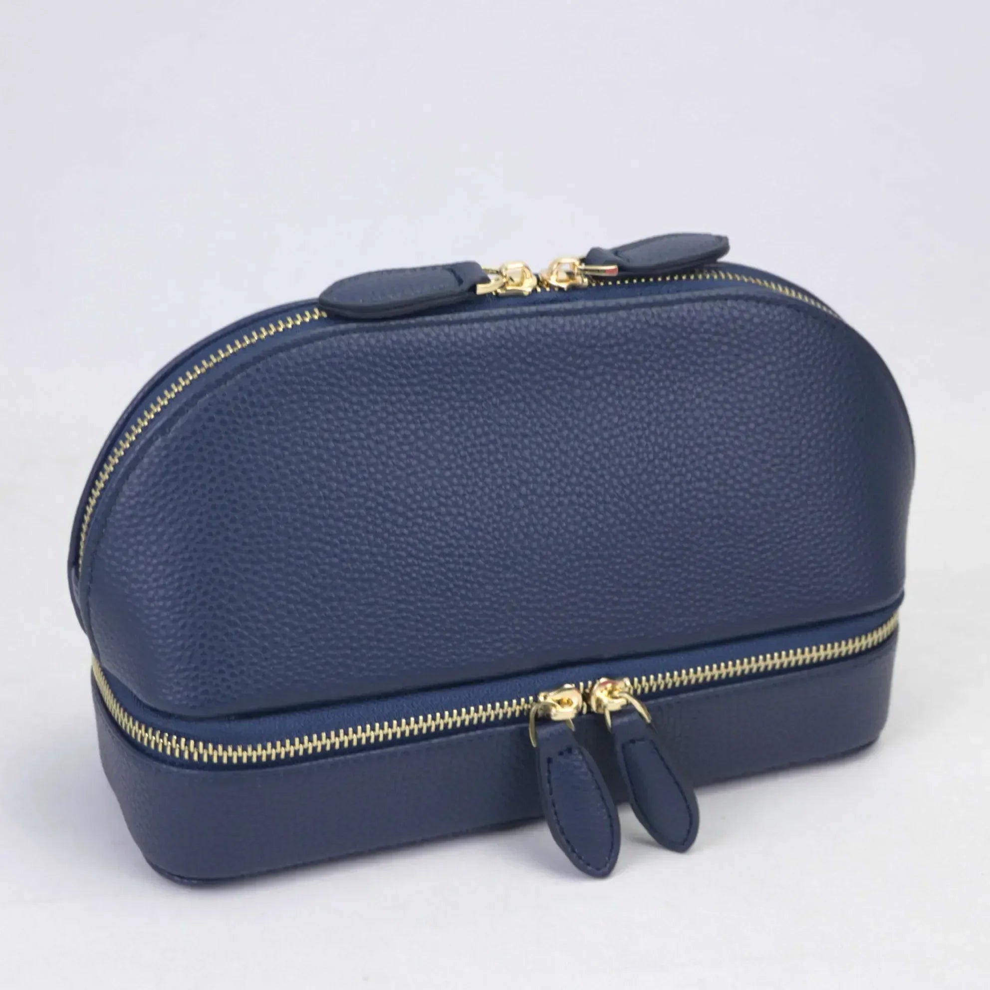 Elegante borsa da toilette in pelle blu scuro con doppia cerniera dorata, design compatto e raffinato, ideale per viaggi e organizzazione.