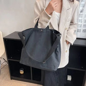 Donna con borsa a tracolla nera in tessuto, indossa giacca beige e maglia bianca. Moda casual, accessori eleganti, outfit autunnale.