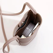Borsa a tracolla in pelle beige, vista dall'alto, con scomparti interni contenenti accessori. Design compatto ed elegante per moda femminile.