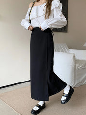 Blusa bianca monospalla con volant, abbinata a gonna lunga nera e mocassini neri con calzini bianchi. Look elegante e moderno per donna.